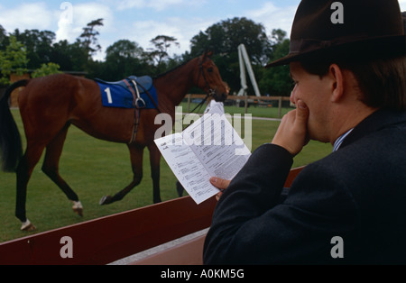 Un parieur lit le tout en étudiant les chevaux racecard de la parade à Salisbury Salisbury en courses, Wiltshire, Royaume-Uni Banque D'Images