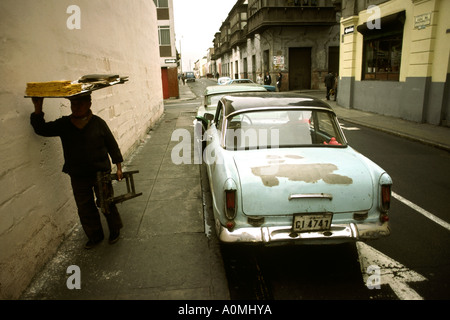 Pérou Lima man carrying tray sur la chaussée sur la tête passé vieille voiture américaine Banque D'Images