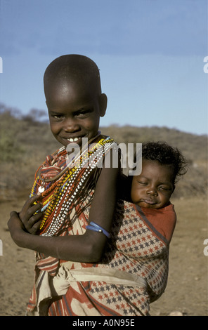 Une fille samburu environ 8 ans porte sa petite sœur dans un tissu papoose sur son dos, près de la réserve nationale de Samburu, Kenya Banque D'Images