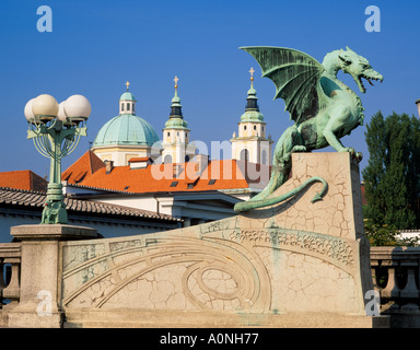 L'un des quatre dragons sur le Pont du Dragon, Ljubljana, Slovénie. Derrière sont les tours de la cathédrale de St Nicolas Banque D'Images