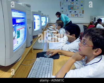 École junior Computer Classroom enfants multiculturels 7-9 ans, avec une enseignante étudient aux écrans de travail dans leur classe d'ordinateur moderne spacieuse Banque D'Images