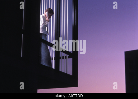Caucasian businessman talking on phone looking out office window dans la nuit Banque D'Images