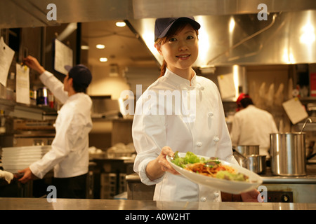 Close up of a waitress holding une assiette de nourriture avec deux serveurs debout dans l'arrière-plan Banque D'Images