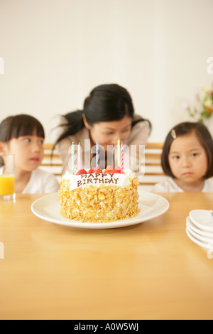 Mid adult woman avec ses filles à la table avec un gâteau d'anniversaire en face d'eux Banque D'Images