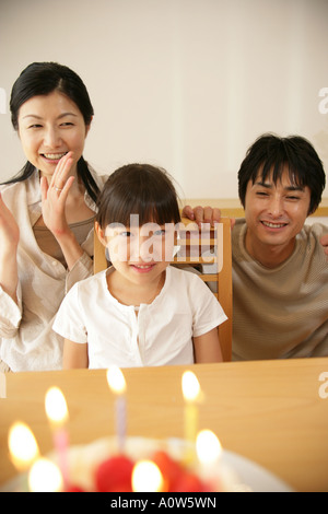 Portrait d'une jeune fille et ses parents assis à une table et des bougies éteintes sur un gâteau d'anniversaire en face d'eux Banque D'Images