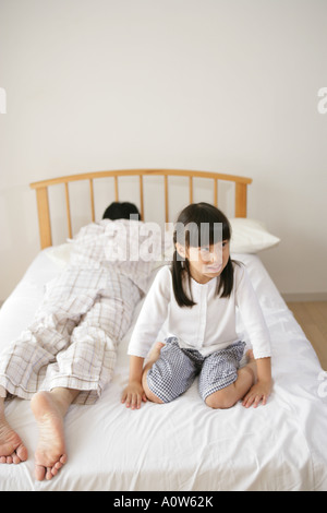Fille assise sur le lit avec son père dormir à côté d'elle Banque D'Images
