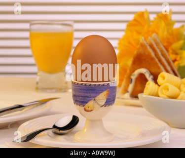 Un petit-déjeuner composé de jus d'orange frais œuf dur et beurrée sur une table ensoleillée lumineux avec des fleurs Banque D'Images