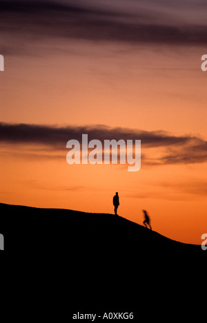 Les randonneurs à pied jusqu'à une colline au coucher du soleil coucher du soleil orange silhouette derrière Banque D'Images