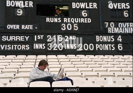 UK Angleterre LONDON Spectator lisant le journal à un match de cricket du comté de tenue à l'Ovale. Tous les sièges vides autour de Banque D'Images