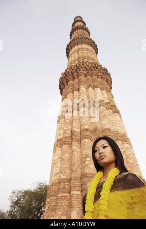 Low angle view of a young woman standing in front of a monument, Qutub Minar, New Delhi, Inde Banque D'Images