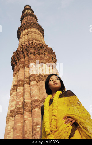 Low angle view of a young woman standing in front of a monument, Qutub Minar, New Delhi, Inde Banque D'Images
