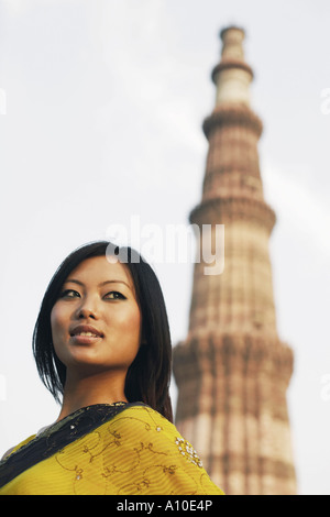 Low angle view of a young woman avec un monument en arrière-plan, Qutub Minar, Delhi, Inde Banque D'Images