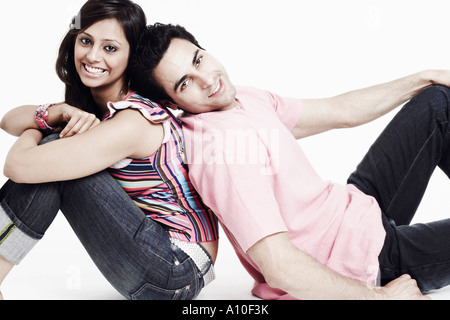 Portrait d'un jeune couple assis dos à dos sur le sol et souriant Banque D'Images