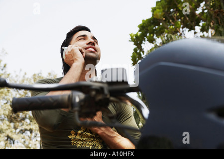 Jeune homme assis sur une moto et en utilisant un téléphone mobile Banque D'Images