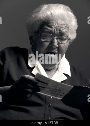 Choqué femme âgée lit lettre ou un paiement de facture contenant des mauvaises nouvelles Banque D'Images