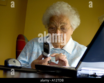 TÉLÉPHONE MOBILE DE PERSONNES ÂGÉES 80-90 ans femme pensive sur appeler ou envoyer des sms avec son téléphone portable lorsqu'il est assis sur un ordinateur portable Banque D'Images