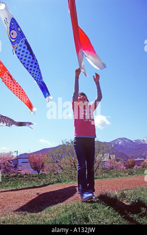 Une jeune fille saute pour attraper battant drapeaux carpe qui représentent la Fête des enfants le 5 mai à Sapporo, Hokkaido, Japon Banque D'Images