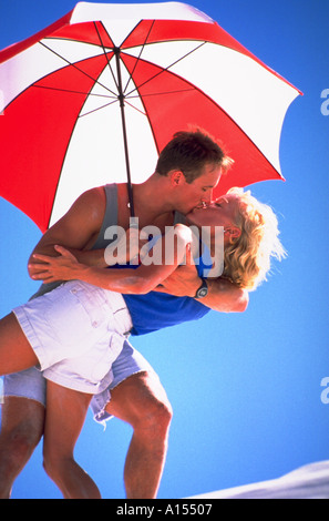 Un homme et une femme s'embrasser passionnément à l'ombre d'un parapluie blanc et rouge Banque D'Images