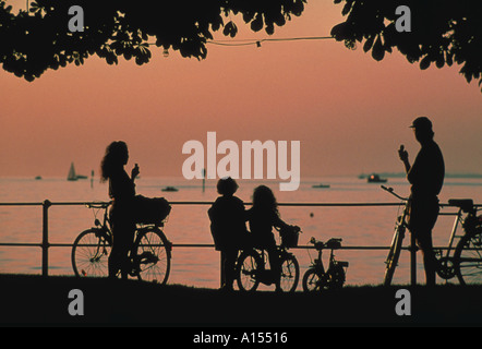 Family on bicycles découpé sur un ciel orange au crépuscule en profitant de la vue et la consommation de crème glacée Banque D'Images