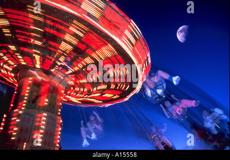 Image floue d'enfants équitation un carrousel swing sur un parc d'amusement avec une demi-lune dans le ciel nocturne dans l'arrière-plan Banque D'Images