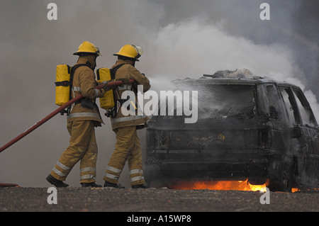 Deux pompiers lutter contre une voiture en flammes. Banque D'Images