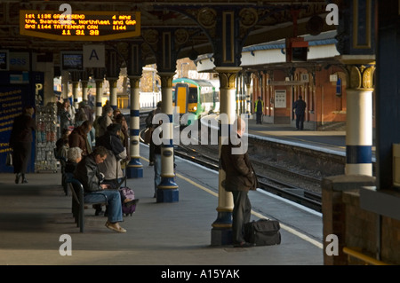 Grand angle horizontal de passagers en attente de trains sur la plate-forme avec une matrice d'information au-dessus de leurs têtes. Banque D'Images