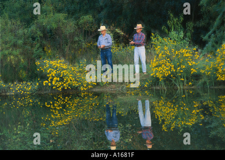 Deux hommes plus âgés, frères, pêche côte à côte, un soir d'été dans les régions rurales de l'étang avec des fleurs sauvages, Missouri USA Banque D'Images