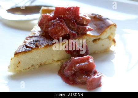 Un morceau de gâteau au fromage au fromage bleu garnie de compote de rhubarbe est sur fond blanc chormé plaque en céramique. Banque D'Images