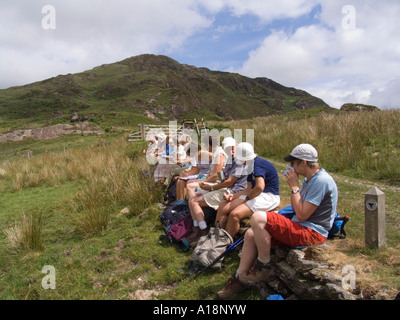 GWYNEDD NORTH WALES UK juillet Groupe de promeneurs assis sur un mur déjeunant par une belle journée ensoleillée lors d'une promenade dans le parc national Eryri Snowdonia Banque D'Images