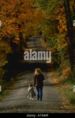 Femme tenant la main de la fillette et marcher le long de route bordée de couleurs d'automne Banque D'Images