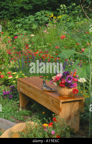 Mobilier en bois fait main banc pin avec panier de fleurs et d'oiseaux du Mexique en céramique peinte dans un jardin de fleurs en fleurs colorées, USA Banque D'Images