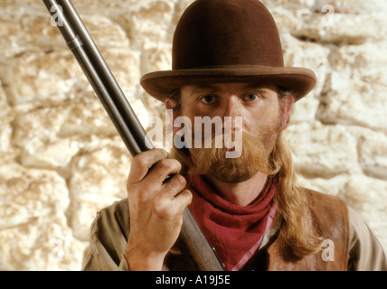 Cowboy avec carabine Winchester contre un mur de pierre blanche Banque D'Images