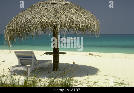 Plage de l'herbe parasol au-dessus d'une chaise longue sur la plage de sable blanc avec de l'eau en barques Bangaram Island Resort Inde Lakshadweep Banque D'Images