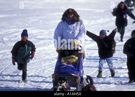 USA Alaska Eskimo Yupik à Unalakleet garçons courir avec musher Martin Buser en ville pendant l'Iditarod Sled Dog Race Banque D'Images