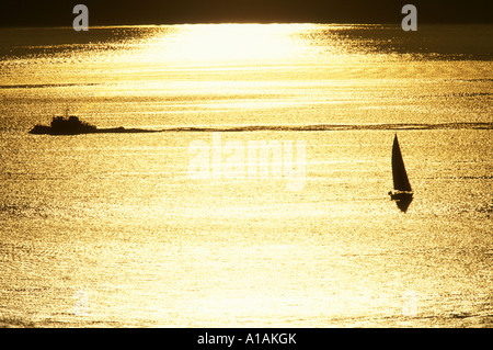 USA Washington Seattle Voilier et passant par la silhouette du remorqueur coucher de soleil le long d'Elliot Bay près de Shilshole Marina Banque D'Images