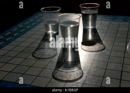 Trois gobelets en plastique transparent de l'eau avec de longues ombres sur une table de café Banque D'Images