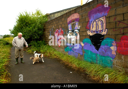 Man Walking dogs passé graffiti art urbain sur le mur d'un bâtiment dans la ville de Newport South Wales UK Banque D'Images