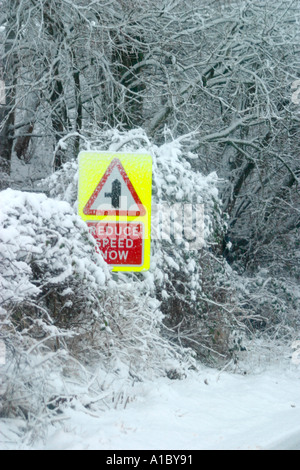 Réduire la vitesse maintenant signer sur côté route sur route enneigée Banque D'Images