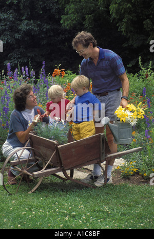 Famille avec deux jeunes enfants jouant dans une antique brouette dans blooming flower garden comme ils le font des travaux extérieurs, Midwest USA Banque D'Images