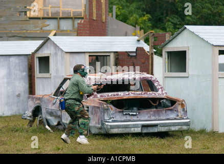 Jeune homme se cachant derrière la voiture tirant sur l'équipe ennemie dans un jeu de paintball Banque D'Images