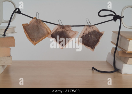 Les sachets de thé le séchage sur une ligne de dentelle attaché par des agrafes, ils sont suspendus entre deux tasses debout sur une pile de livres Banque D'Images