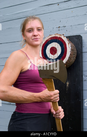 Jeune femme tenant son concurrent en bois massif ax à côté d'une cible de lancement de hache lors d'une foire dans le Connecticut, USA. Banque D'Images