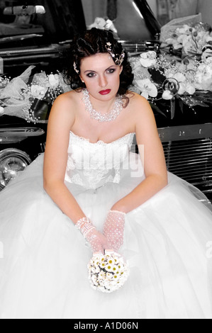 Jeune femme mariée solitaire en robe de mariage de l'emplacement sur une voiture Banque D'Images