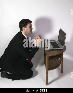 L'homme d'affaires à genoux priant à son ordinateur portable Banque D'Images