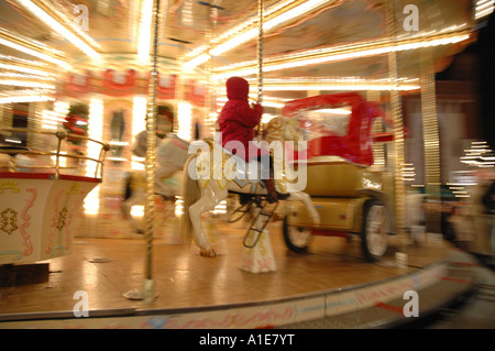 Enfant en anorak rouge se déplace sur un cheval de bois pour enfant-carousel sur le marché de Noël Banque D'Images