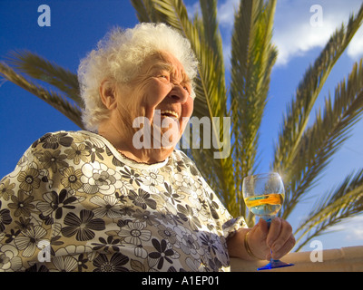 Femme âgée détend rire joyeusement dans le soleil avec un verre de vin blanc dans sa villa de vacances home Banque D'Images