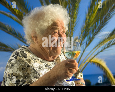 Femme âgée se détend avec contentement au soleil avec un verre de vin blanc dans sa villa de vacances home Banque D'Images