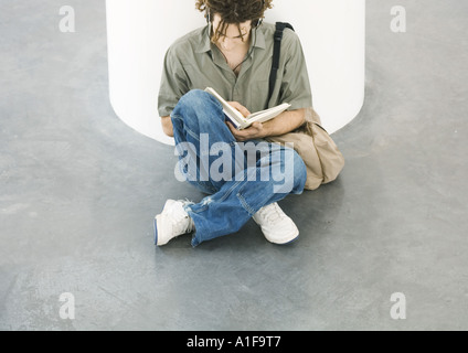 Jeune homme assis sur le plancher, la lecture Banque D'Images