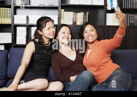 Close-up of a Mid adult woman sitting avec deux jeunes femmes sur un canapé en prenant une photo d'eux Banque D'Images