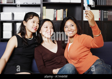 Close-up of a Mid adult woman sitting avec deux jeunes femmes sur un canapé en prenant une photo d'eux Banque D'Images